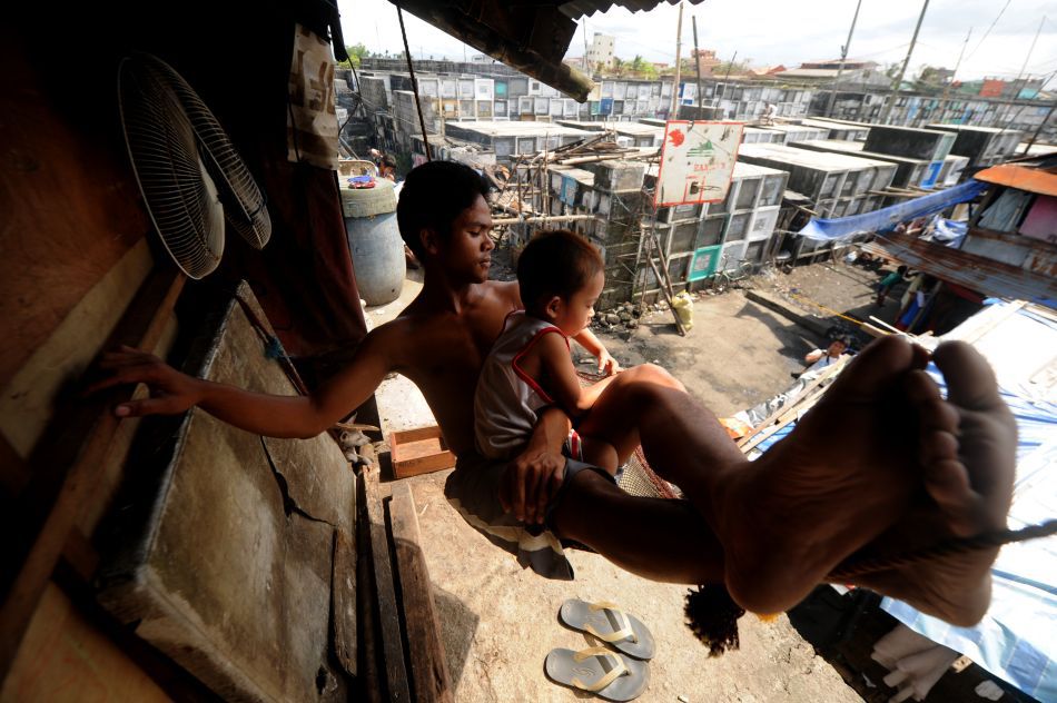 Un bărbat se odihneşte împreună cu fiul său într-un hamac în casa lor din Cimitirului Municipal din Manila (Filipine), 30 Octombrie 2011